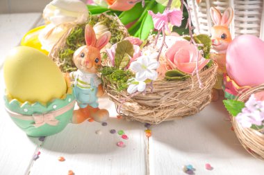  Yuvalar, renkli yumurtalar, tavşanlar ve bahar çiçekleri olan mutlu paskalya konsepti. Güneşli ahşap arka planda tebrik kartı 