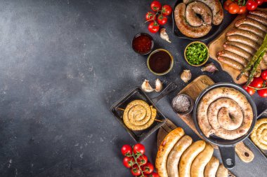 Assortment of different fried sausages. Set with various meat Bavarian, Frankfurt, German grilled sausages, Oktoberfest or summer BBQ party concept, bkack concrete background copy space top view