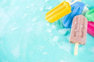 Çok renkli, parlak dondurmalı buzlu dondurma seçimi. Çeşitli dondurmalar, dondurulmuş lolipoplar. Çikolatalı, vanilyalı, böğürtlenli, fıstıklı, portakallı, açık mavi, güneşli arka planda ezilmiş buzlu.