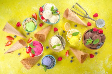 Farklı kaselerde çeşitli renkli dondurma topları, dondurma külahları ve aromalı malzemeler - şam fıstığı, böğürtlen, limon, çikolata, vanilya, nane. Renkli sarı parlak arkaplan