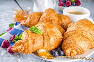 Kahve fincanı, portakal reçeli ve taze yaz meyveli tatlı tereyağlı kruvasan. Ayçöreği kavramlı geleneksel kıtasal kahvaltı, gri taş arka plan kopyalama alanı