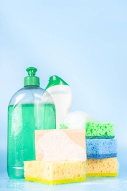 Bahar temizliği, temizlik konsepti, çeşitli parlak temizlik malzemeleri, şişeler, çatal bıçaklar, malzemeler. Açık mavi arkaplanda sabun köpükleri ve köpük, kopyalama alanı