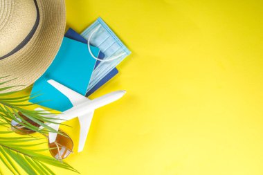 Oyuncak uçak, tropik tatil dekorasyonu ve aksesuarlar, yüz maskesi, sarı parlak arka planda antiseptik sprey. Coronavirus salgını sırasında seyahat etmek. Covid-19 aşı pasaport kartı