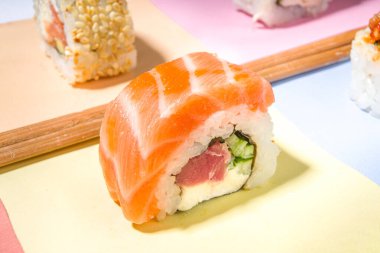 Pilav, balık ve çubuklarla hazırlanmış suşi ruloları çeşitli renkli parlak arka planlar, modaya uygun koyu gölgeler.