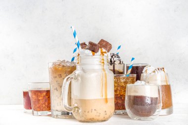 Farklı buzlu yaz kahve içecekleri - espresso, frappe, latte, cappuccino, kremalı, şuruplu ve ezilmiş buzlu, çeşitli bardaklarda ve kupalarda beyaz arka planda fotokopi alanı