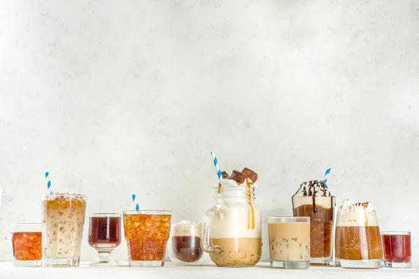 Set with different iced summer coffee drinks - espresso, frappe, latte, cappuccino, with whipped cream, syrup and crushed ice, in various glasses and  mugs on white background copy space