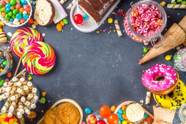 Renkli şekerlerden seç. Çeşitli şekerler, çikolatalar, çörekler, kurabiyeler, lolipoplar, siyah beton arka planda dondurma üst görünümü