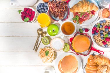 Çeşitli geleneksel kahvaltı yemekleri - domuz pastırmalı kızarmış yumurta, müsli, yulaf, waffle, gözleme, burger, kruvasan, meyve üzümü, kahve, çay ve portakal suyu, beyaz masa arkaplan fotokopisi