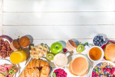 Çeşitli geleneksel kahvaltı yemekleri - domuz pastırmalı kızarmış yumurta, müsli, yulaf, waffle, gözleme, burger, kruvasan, meyve üzümü, kahve, çay ve portakal suyu, beyaz masa arkaplan fotokopisi