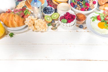 Çeşitli geleneksel kahvaltı yemekleri - domuz pastırmalı kızarmış yumurta, müsli, yulaf, waffle, gözleme, burger, kruvasan, meyve üzümü, kahve, çay ve portakal suyu, beyaz masa arkaplan fotokopisi