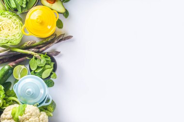 Çeşitli organik yeşil baharatlı sebze malzemeleri beyaz mutfak masasında porsiyonlu tencereler, üst manzara. Diyet sağlıklı çorba, güveç yemek hazırlama konsepti