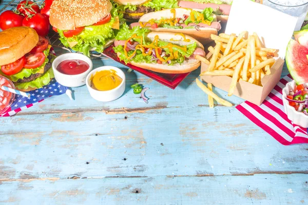 Fourth of July, Memorial Day, USA Independence Day concept. Patriotic, American traditional food. Picnic party with watermelon, burgers, hot dogs, drinks, blue wooden outdoor table background