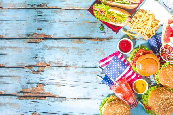 7月4日 アメリカ独立記念日のコンセプト 愛国的で伝統的なアメリカ料理 スイカ ハンバーガー ホットドッグ 飲み物 青い木製の屋外テーブルの背景を持つピクニックパーティー — ストック写真
