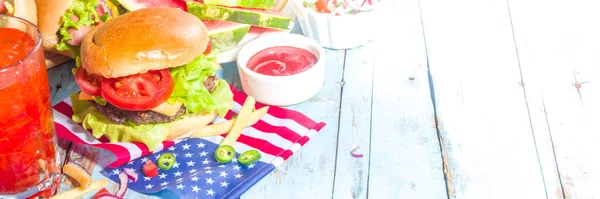 Fourth of July, Memorial Day, USA Independence Day concept. Patriotic, American traditional food. Picnic party with watermelon, burgers, hot dogs, drinks, blue wooden outdoor table background