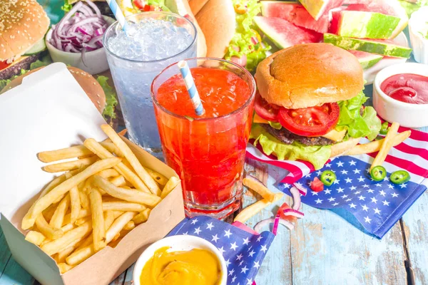 Fourth of July, Memorial Day, USA Independence Day concept. Patriotic, American traditional food. Picnic party with watermelon, burgers, hot dogs, drinks, blue wooden outdoor table background