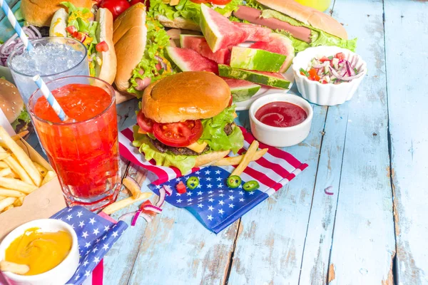 Fourth of July, Memorial Day, USA Independence Day concept. Patriotic, American traditional food. Picnic party with watermelon, burgers, hot dogs, drinks, blue wooden outdoor table background