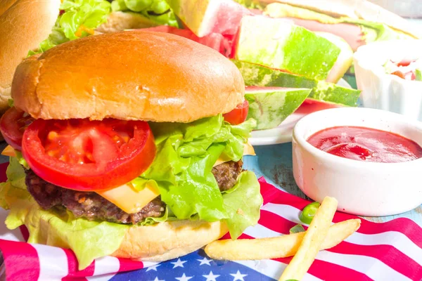 Fourth of July, Memorial Day, USA Independence Day concept. Patriotic, American traditional food. Picnic party with watermelon, burgers, hot dogs, drinks, blue wooden outdoor table background