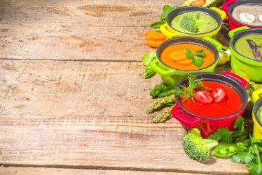 Çeşitli renkte sebze çorbaları. Küçük porsiyonlu kuşkonmaz, ıspanak, brokoli, yeşil bezelye, domates, havuç gibi çeşitli sebze kremalı çorbalar. Ahşap arkaplan kopyalama alanı üst görünümü