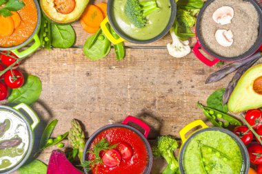 Çeşitli renkte sebze çorbaları. Küçük porsiyonlu kuşkonmaz, ıspanak, brokoli, yeşil bezelye, domates, havuç gibi çeşitli sebze kremalı çorbalar. Ahşap arkaplan kopyalama alanı üst görünümü