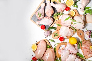 Çeşitli çiğ tavuk eti porsiyonları. Pişmemiş tavuk filetosu, but, kanatlar, şeritler ve bacaklar beyaz yemek masasında baharatlı. 