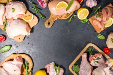 Çeşitli çiğ tavuk eti porsiyonları. Pişmemiş tavuk filetosu, but, kanatlar, şeritler ve bacaklar siyah yemek masasında baharatlı. 