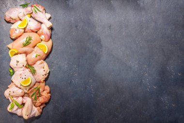 Çeşitli çiğ tavuk eti porsiyonları. Pişmemiş tavuk filetosu, but, kanatlar, şeritler ve bacaklar siyah yemek masasında baharatlı. 