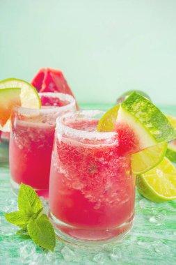 Soğuk yaz kokteyli, karpuz margaritası ya da karpuz ve limon dilimleri, ezilmiş buz ve naneli mojito. Parlak yeşil güneşli arka planda mevsimlik ferahlatıcı içecekler