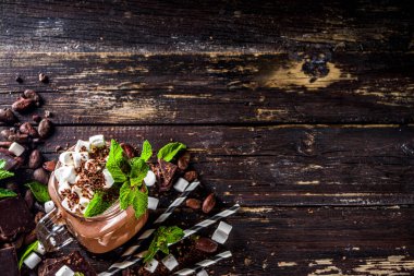 Soslu çikolatalı milkshake, şekerleme ve naneli rendelenmiş çikolata. Bir sürü çikolata, kakao çekirdeği ve çikolata parçacıklarıyla dolu eski bir kırsal ahşap masada.