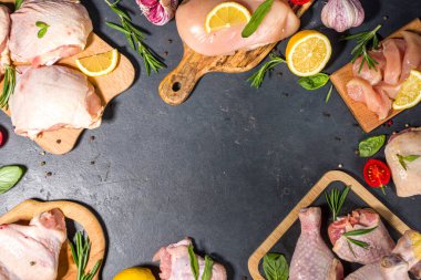 Çeşitli çiğ tavuk eti porsiyonları. Pişmemiş tavuk filetosu, but, kanatlar, şeritler ve bacaklar siyah yemek masasında baharatlı. 