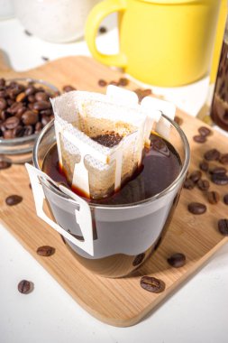 Poşetten taze demlenmiş bir fincan kahve. Süslü kahve çeşitleri, beyaz mutfak masasında fincanlar, kopyalama alanı