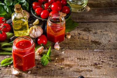 Fesleğen, sarımsak ve taze domatesli ev yapımı domates sosu. Ketçap, küçük kavanozlarda marinara sosu. Tahta bir arka planda, taze sebze ve fesleğenle.