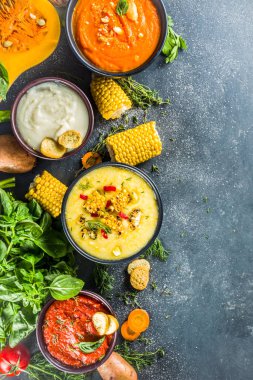 Farklı sonbahar çorbaları seti. Portakal kaselerinde çeşitli sebze çorbaları - mısır, patates, balkabağı, domates, kabak, brokoli kremalı çorba. Siyah beton arkaplanda üst görünüm kopyalama alanı