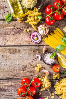 Çeşitli çiğ makarna ve baharatlar. Taze otlar ve sebzelerle İtalyan makarnası pişirmek. Rustik biçim, ahşap arkaplan üst görünüm kopyalama alanı