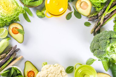 Çeşitli organik yeşil baharatlı sebze malzemeleri beyaz mutfak masasında porsiyonlu tencereler, üst manzara. Diyet sağlıklı çorba, güveç yemek hazırlama konsepti