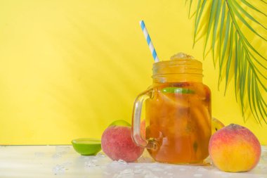 Yaz serinletici içecek, geleneksel buzlu şeftali çayı kokteyli ezilmiş buz, şeftali dilimleri ve limon, parlak, güneşli, meyveli ve tropikal yapraklı arka planda