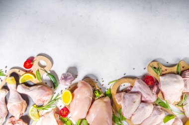 Çeşitli çiğ tavuk eti porsiyonları. Pişmemiş tavuk filetosu, but, kanatlar, şeritler ve bacaklar beyaz yemek masasında baharatlı. 