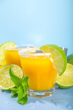 Soğuk yaz kokteyli, tekila, tuzlu limon dilimleri, ezilmiş buz ve naneli mango margaritası. Sezonluk ferahlatıcı bir içecek, parlak mavi güneş arka planda.