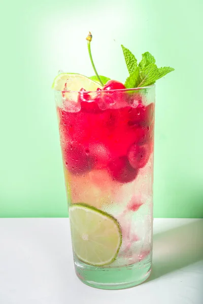 冷たくてさわやかな夏の飲み物 チェリーコーラ リメイド モヒートレモネードカクテルライムとチェリーのカラフルな明るい緑の背景 — ストック写真