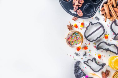 Cadılar Bayramı zencefilli kurabiye pişirme arka planı. Sonbahar tatili pişirme konsepti, malzemeler, baharatlar, cadılar bayramı sembolü kurabiye kesiciler - balkabağı, hayalet, yarasa, cadı şapkası, üst görünüm beyaz masa kopyalama alanı