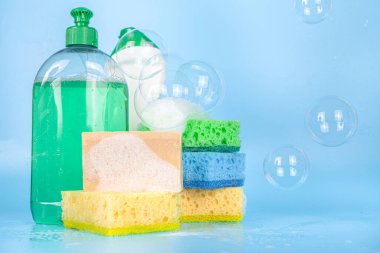 Bahar temizliği, temizlik konsepti, çeşitli parlak temizlik malzemeleri, şişeler, çatal bıçaklar, malzemeler. Açık mavi arkaplanda sabun köpükleri ve köpük, kopyalama alanı
