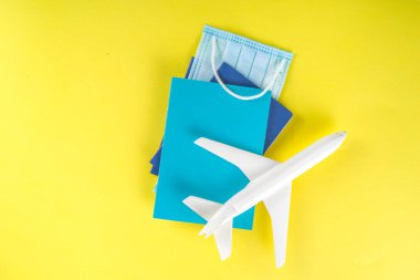 Oyuncak uçak, tropik tatil dekorasyonu ve aksesuarlar, yüz maskesi, sarı parlak arka planda antiseptik sprey. Coronavirus salgını sırasında seyahat etmek. Covid-19 aşı pasaport kartı