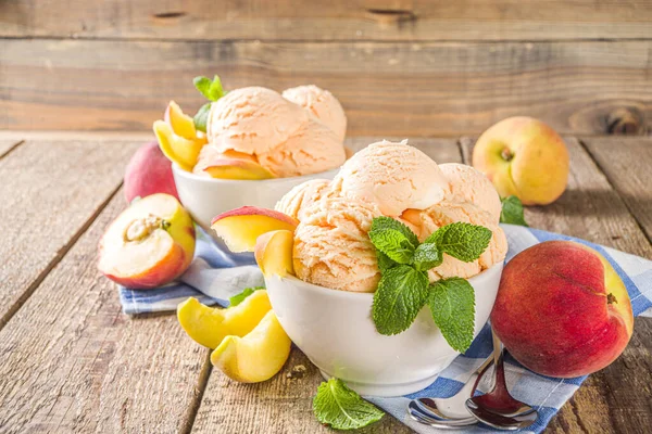 Homemade sweet peach ice cream. Peach gelato balls in small bowls, on wooden background with fresh peaches and mint leaves