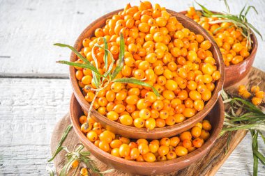  Küçük organik ahşap kasede deniz dikenli üzümler, beyaz ahşap masa arka planında deniz dikenli dallar