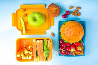 Okula dönmek, sağlıklı, lezzetli çocuk beslenme çantası sandviç, fındık, taze meyve ve sebze çubukları. Okul gereçleri, kalemler, defterler, parlak mavi arkaplan düz arkaplan üst görünüm kopyalama alanı