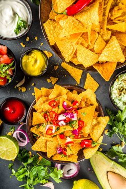 Eritilmiş peynirli cips ve çeşitli geleneksel Meksika sosları, salsa ve jalapeno, koyu gri arka plan fotokopi alanı
