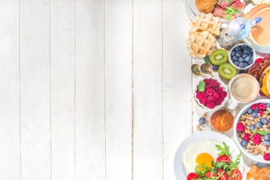 Çeşitli geleneksel kahvaltı yemekleri - domuz pastırmalı kızarmış yumurta, müsli, yulaf, waffle, gözleme, burger, kruvasan, meyve üzümü, kahve, çay ve portakal suyu, beyaz masa arkaplan fotokopisi