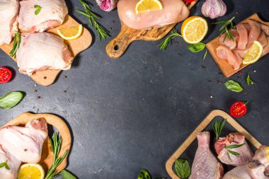 Çeşitli çiğ tavuk eti porsiyonları. Pişmemiş tavuk filetosu, but, kanatlar, şeritler ve bacaklar siyah yemek masasında baharatlı. 