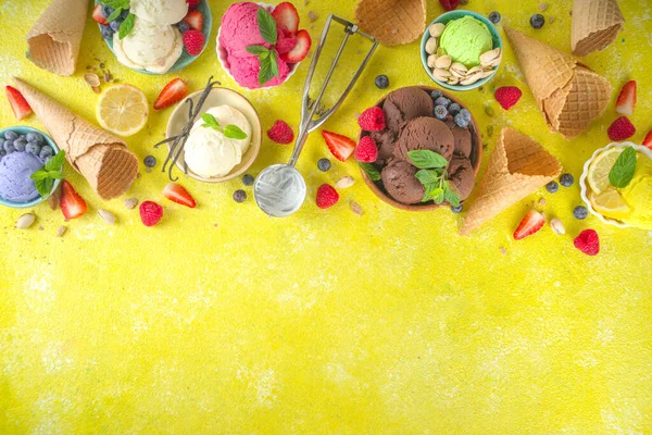 Farklı kaselerde çeşitli renkli dondurma topları, dondurma külahları ve aromalı malzemeler - şam fıstığı, böğürtlen, limon, çikolata, vanilya, nane. Renkli sarı parlak arkaplan