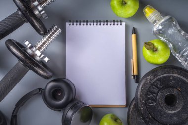 Koyu demir halterleri, spor ayakkabıları, kulaklıkları, rendelenmiş elmaları ve su şişeleri olan erkekler fitness geçmişi. Gri arkaplan üstü görünümü kopyalama alanı