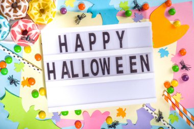 Parlak renkli maket parti davetiyesi, menü, Cadılar Bayramı için tebrik kartı. Kâğıt cadılar bayramı sembolleri hayaletler, yarasalar, şekerler, kokteyl tüpleri olan renkli bir arka plan. Üst görünüm çerçeve kopyalama alanı